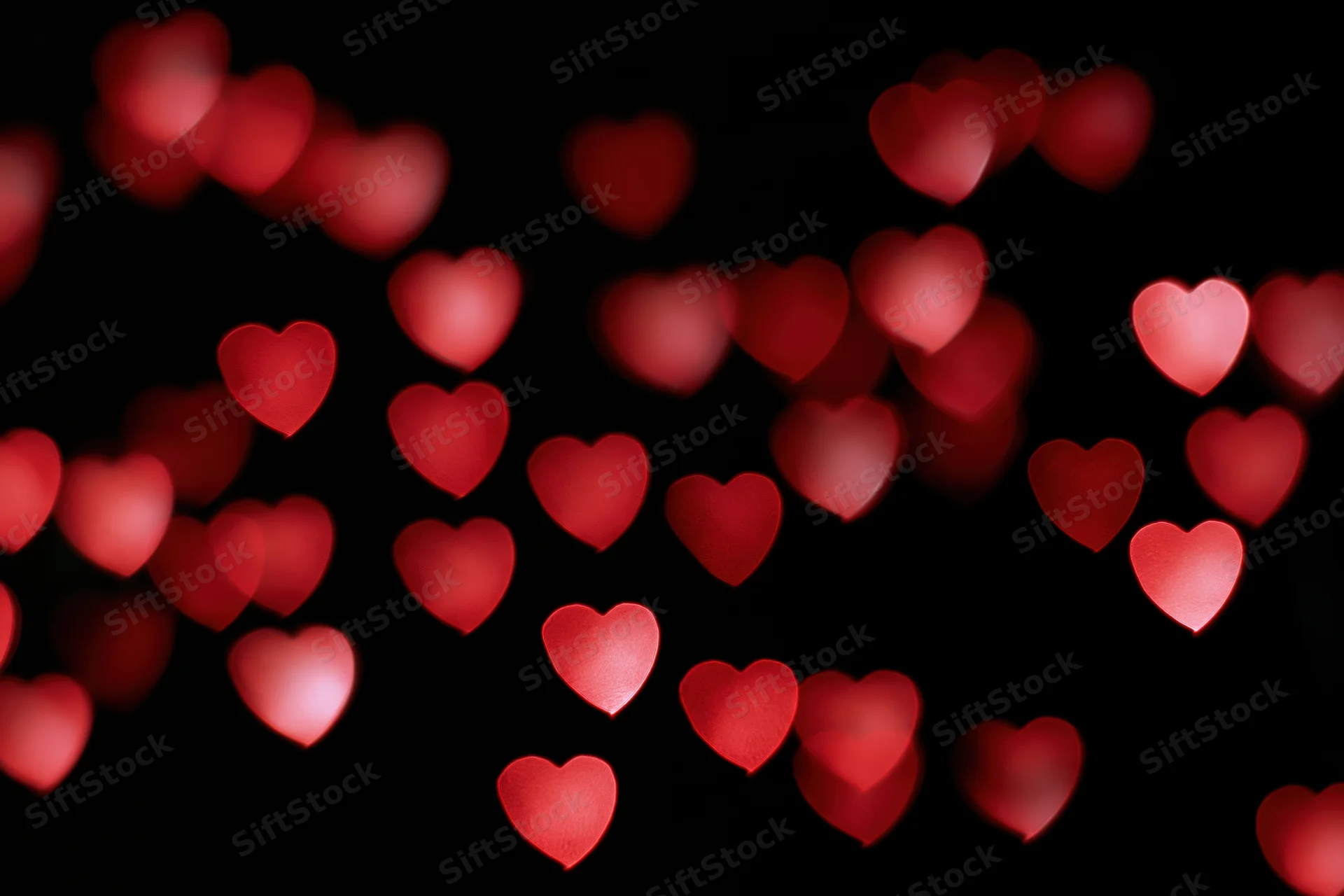 Red heart-shaped bokeh lights scattered across a black background