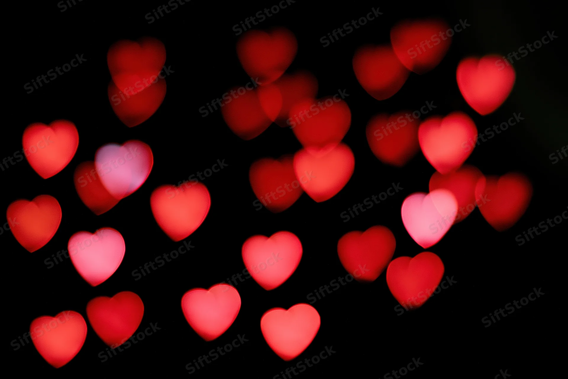 Red heart-shaped bokeh lights scattered across a black background