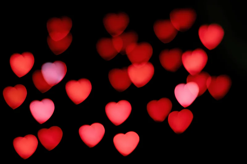 Red heart-shaped bokeh lights scattered across a black background