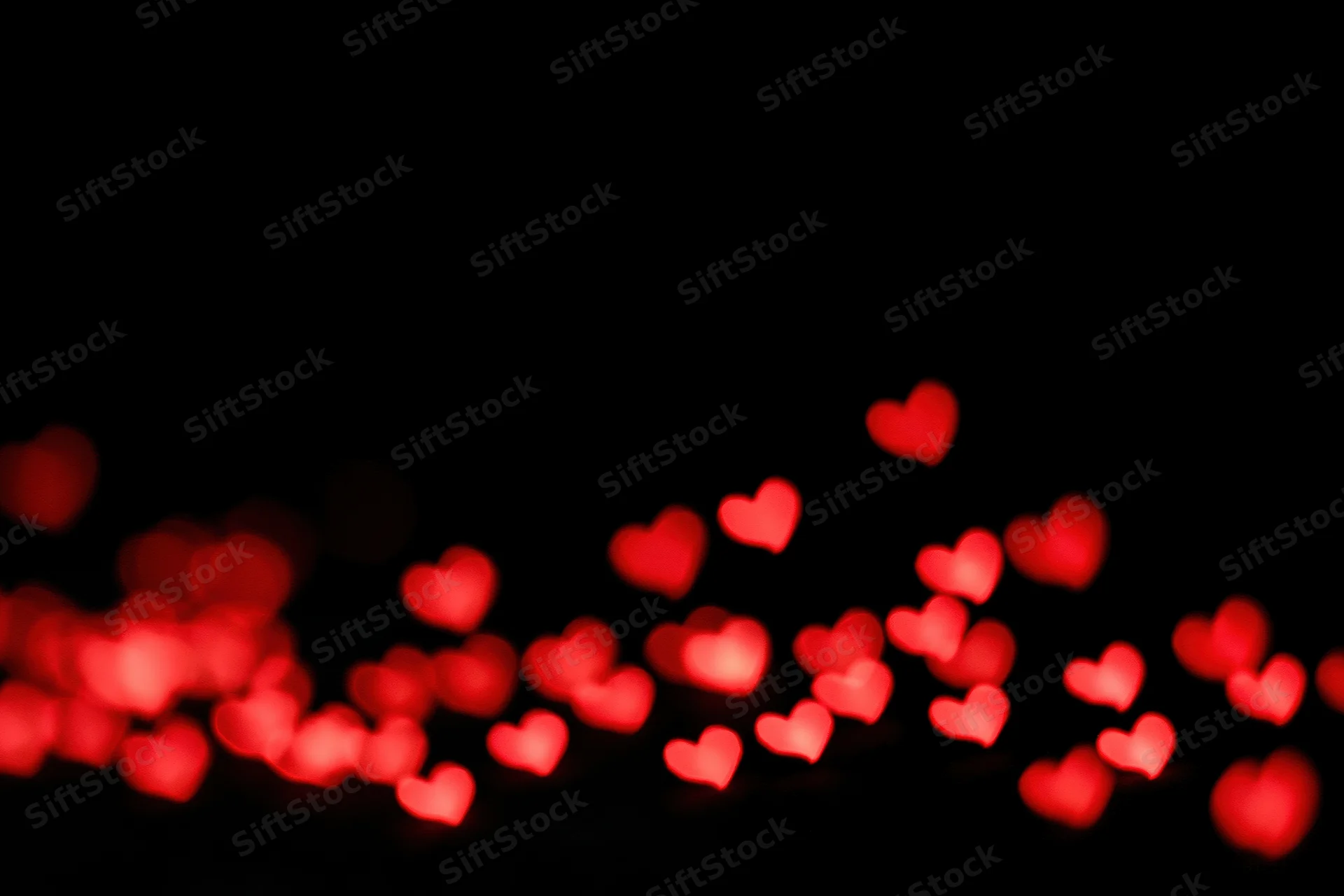 Red heart-shaped bokeh lights scattered across the lower part of a dark background