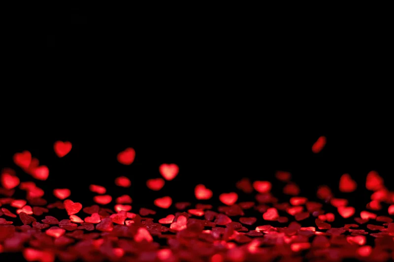 Red heart-shaped bokeh lights scattered across the lower portion of a black background
