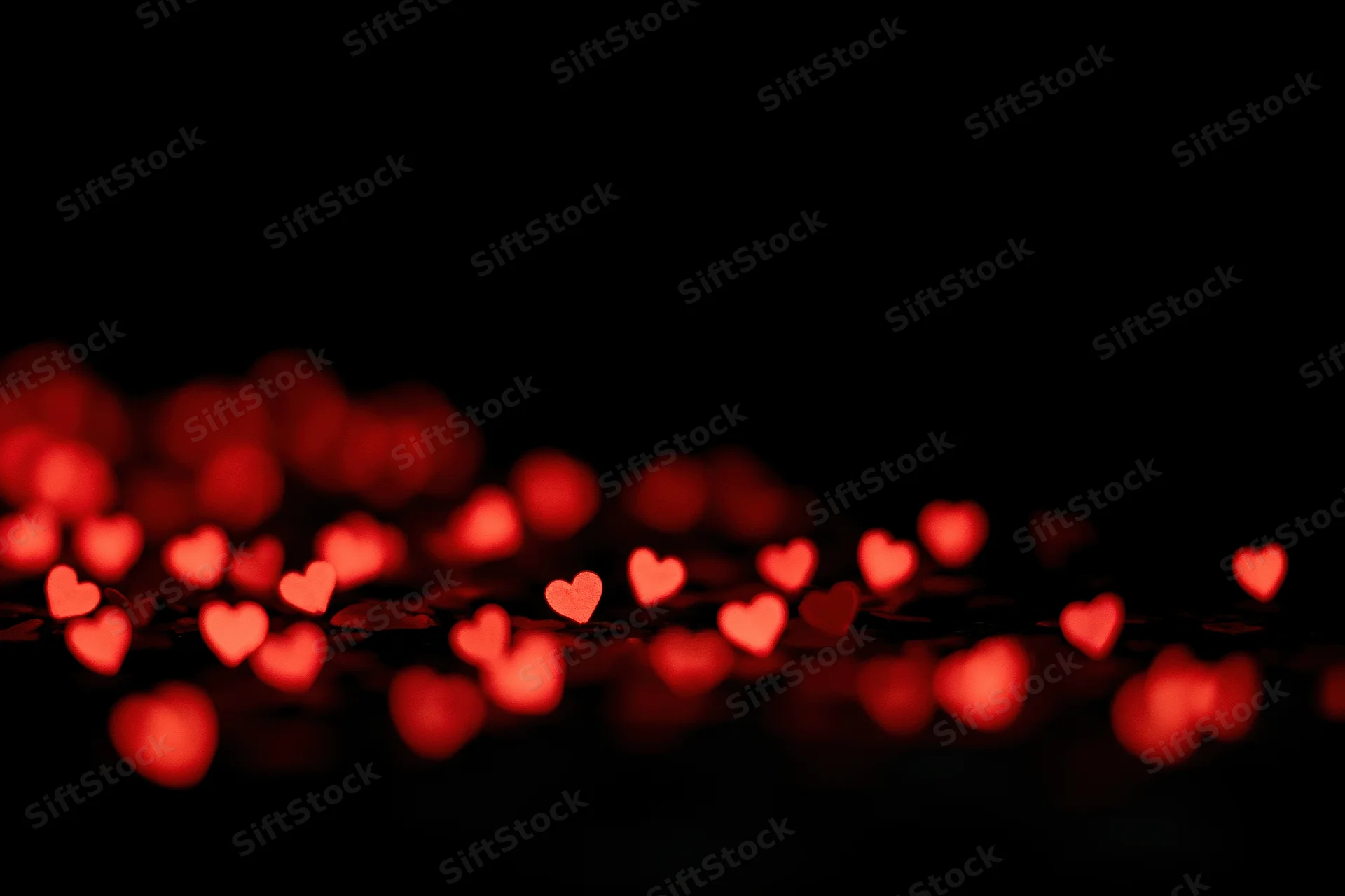 Red heart-shaped bokeh lights scattered across the lower portion of a dark background