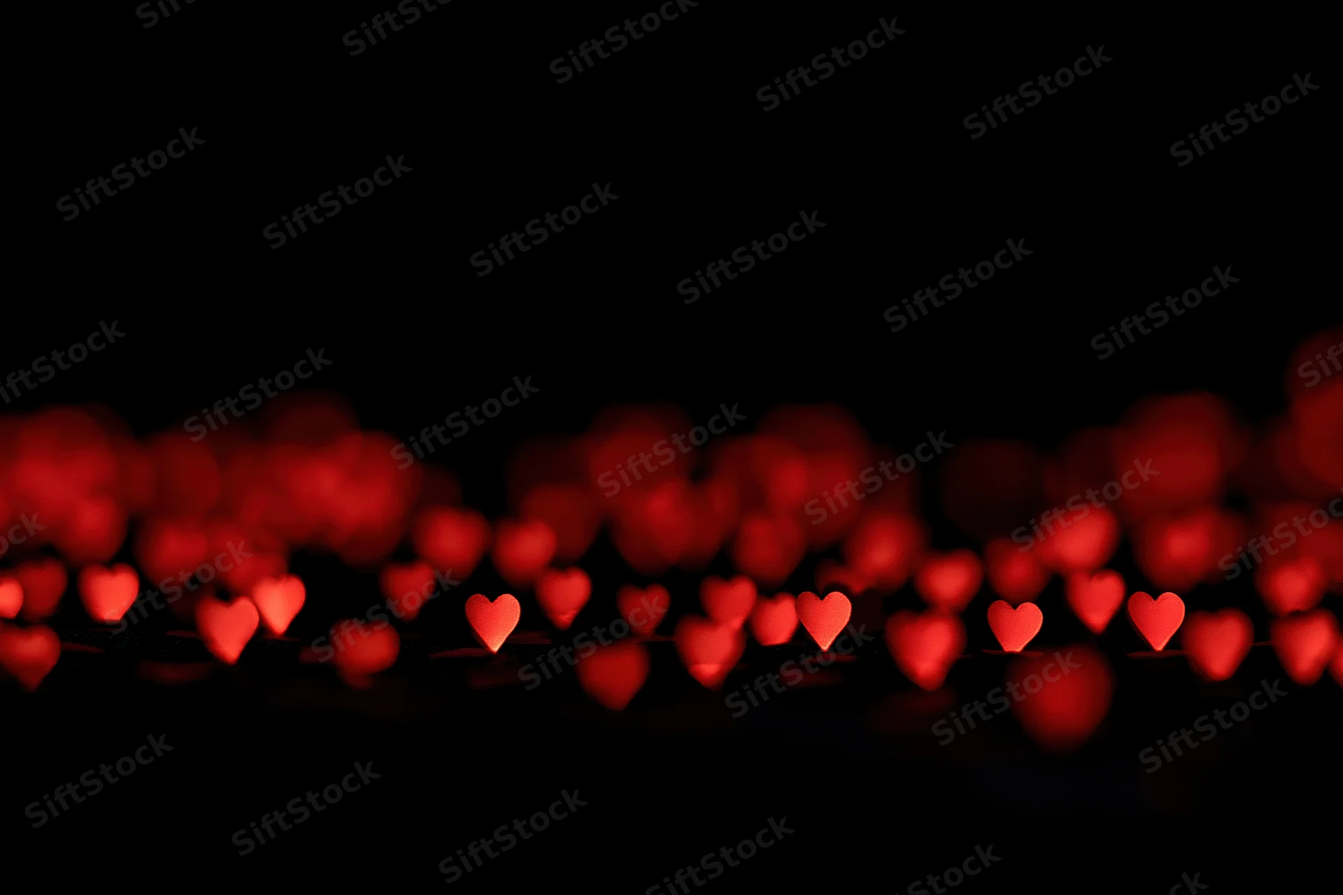 Red heart-shaped bokeh lights scattered across the lower portion of a dark frame