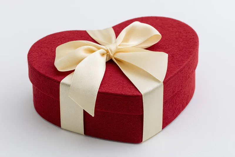 Red heart-shaped gift box with cream satin ribbon tied in a bow on white background