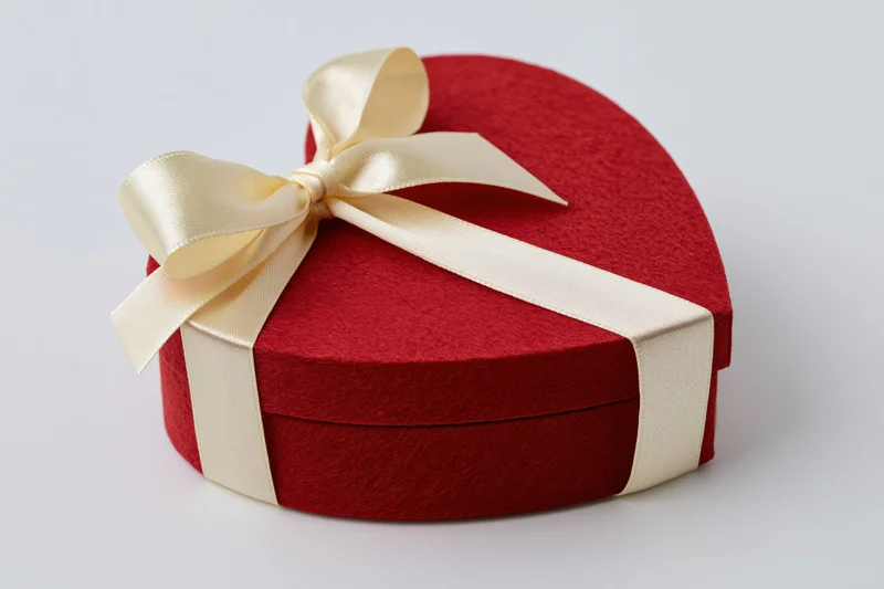 Red heart-shaped gift box wrapped with cream satin ribbon on white background