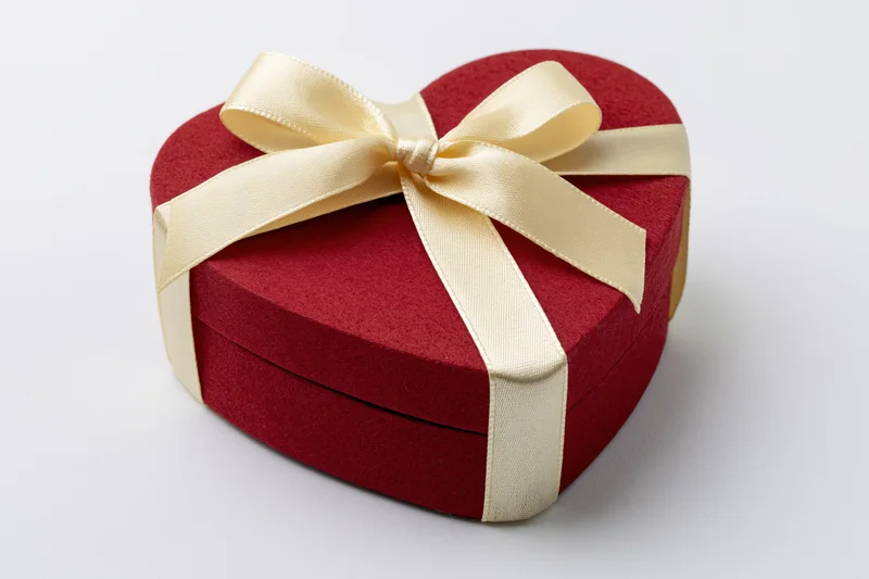 Red heart-shaped gift box wrapped with cream satin ribbon on white background