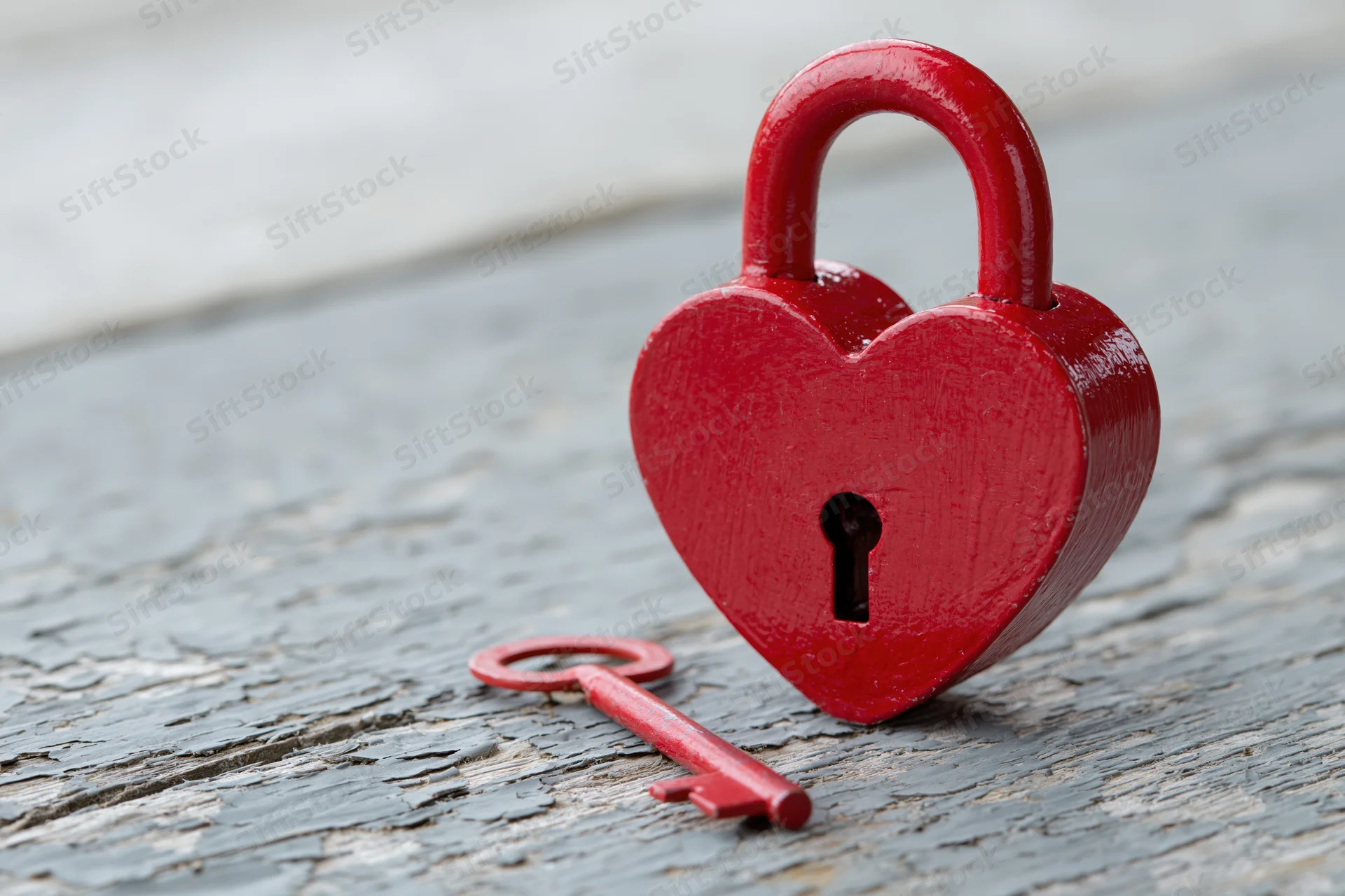 Red heart-shaped padlock with matching key resting on weathered wooden surface