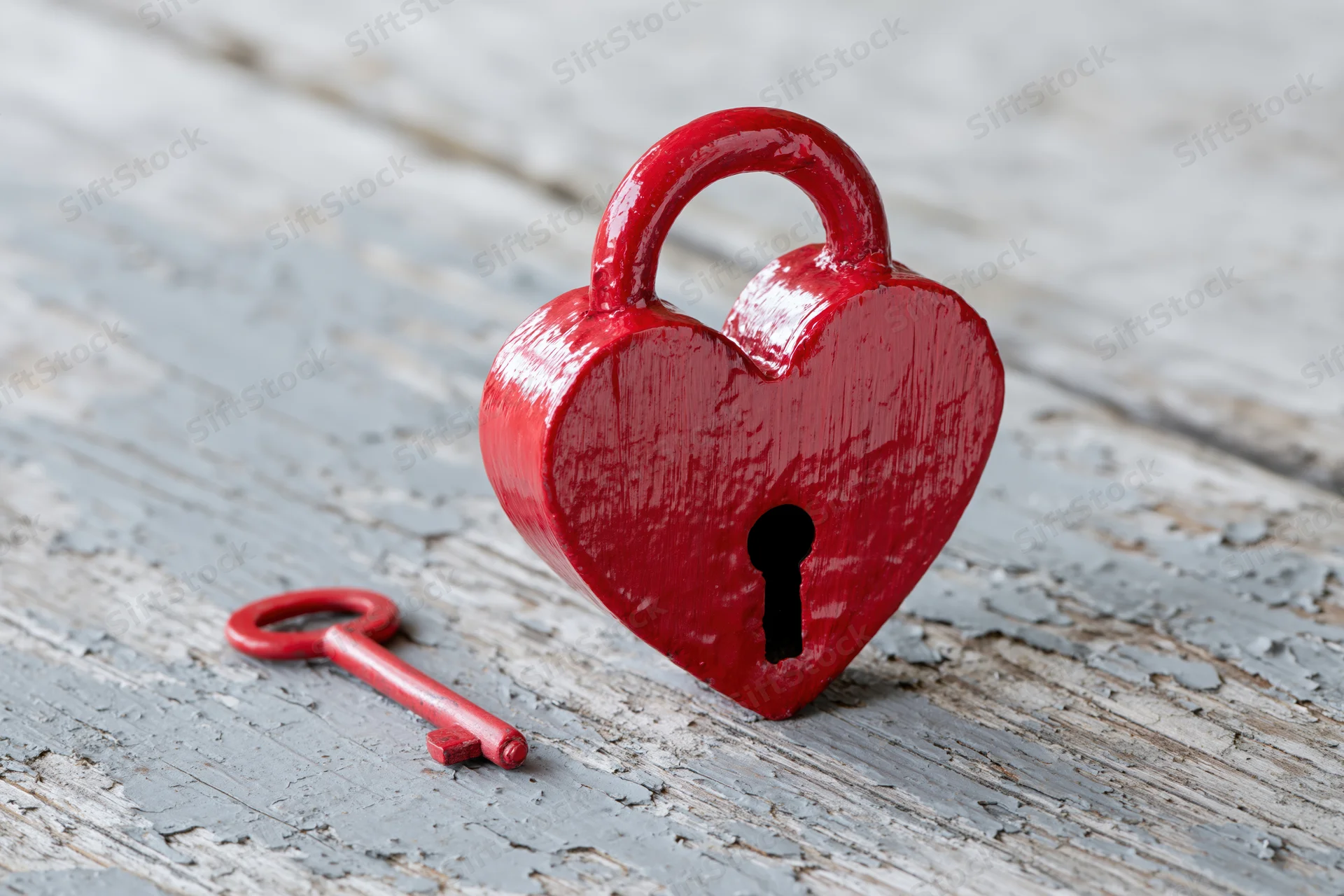 Red heart-shaped lock with matching key on weathered wooden surface
