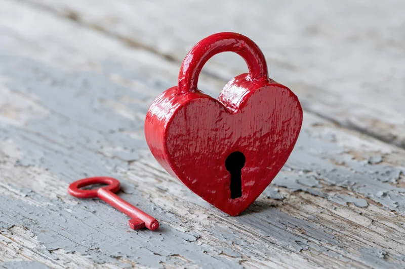 Red heart-shaped lock with matching key on weathered wooden surface