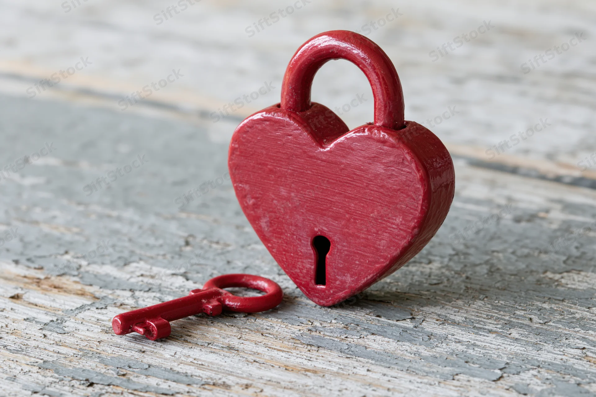 Red heart-shaped padlock with matching key resting on weathered wooden surface
