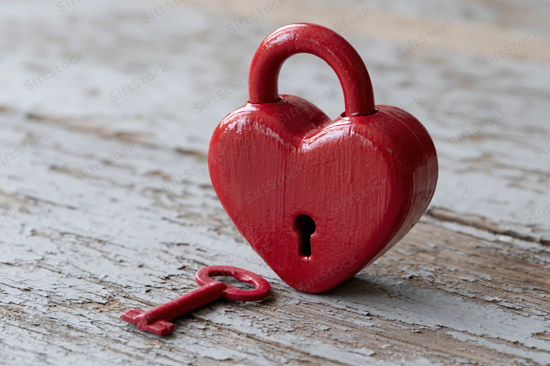 Red heart-shaped lock with matching key on weathered wooden surface