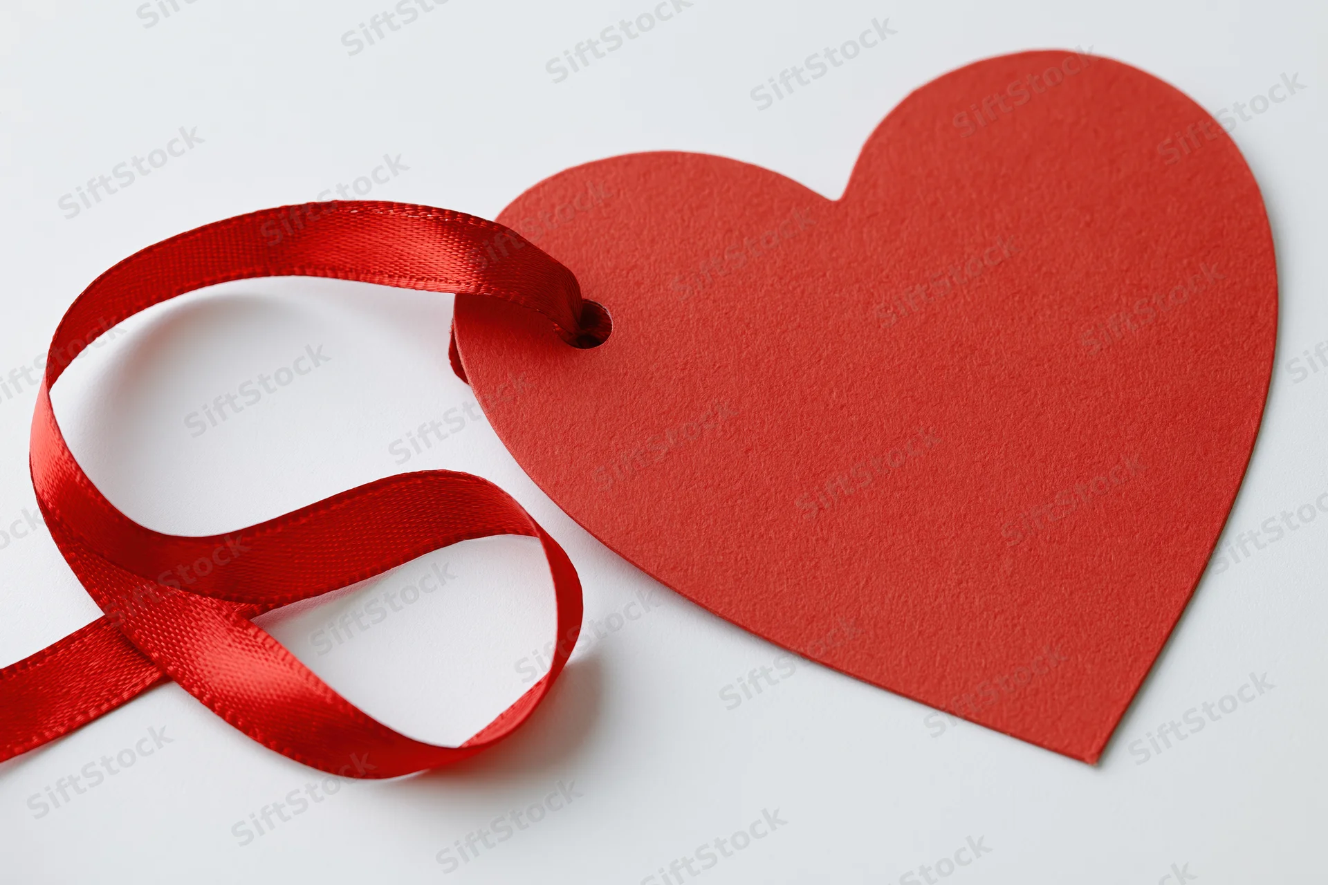 Red heart-shaped paper gift tag with a red satin ribbon loop on white background