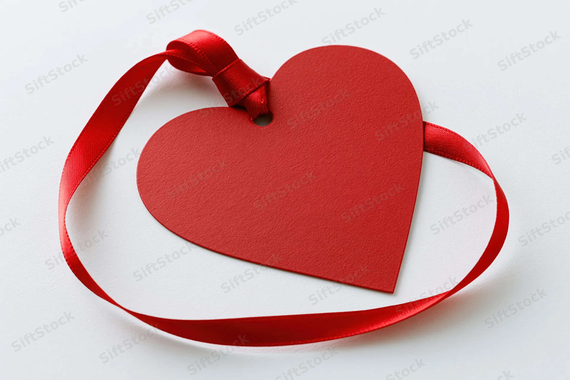 Red heart-shaped paper gift tag with a red satin ribbon loop on white background