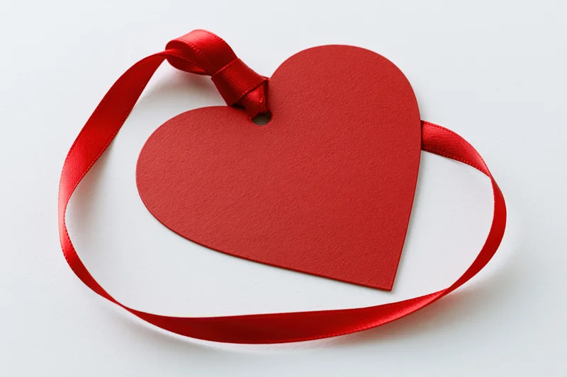 Red heart-shaped paper gift tag with a red satin ribbon loop on white background