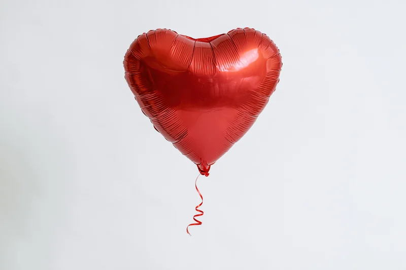 Red metallic heart-shaped foil balloon floating against a plain white background