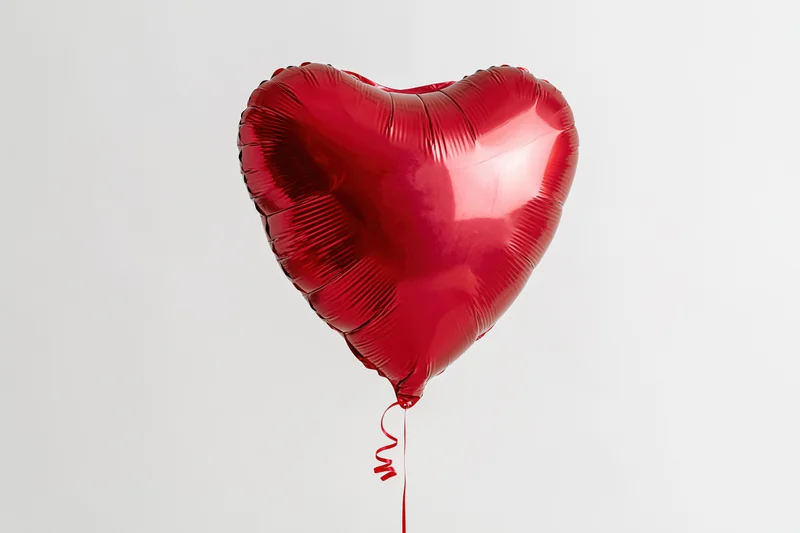 Red metallic heart-shaped foil balloon floating against a plain white background