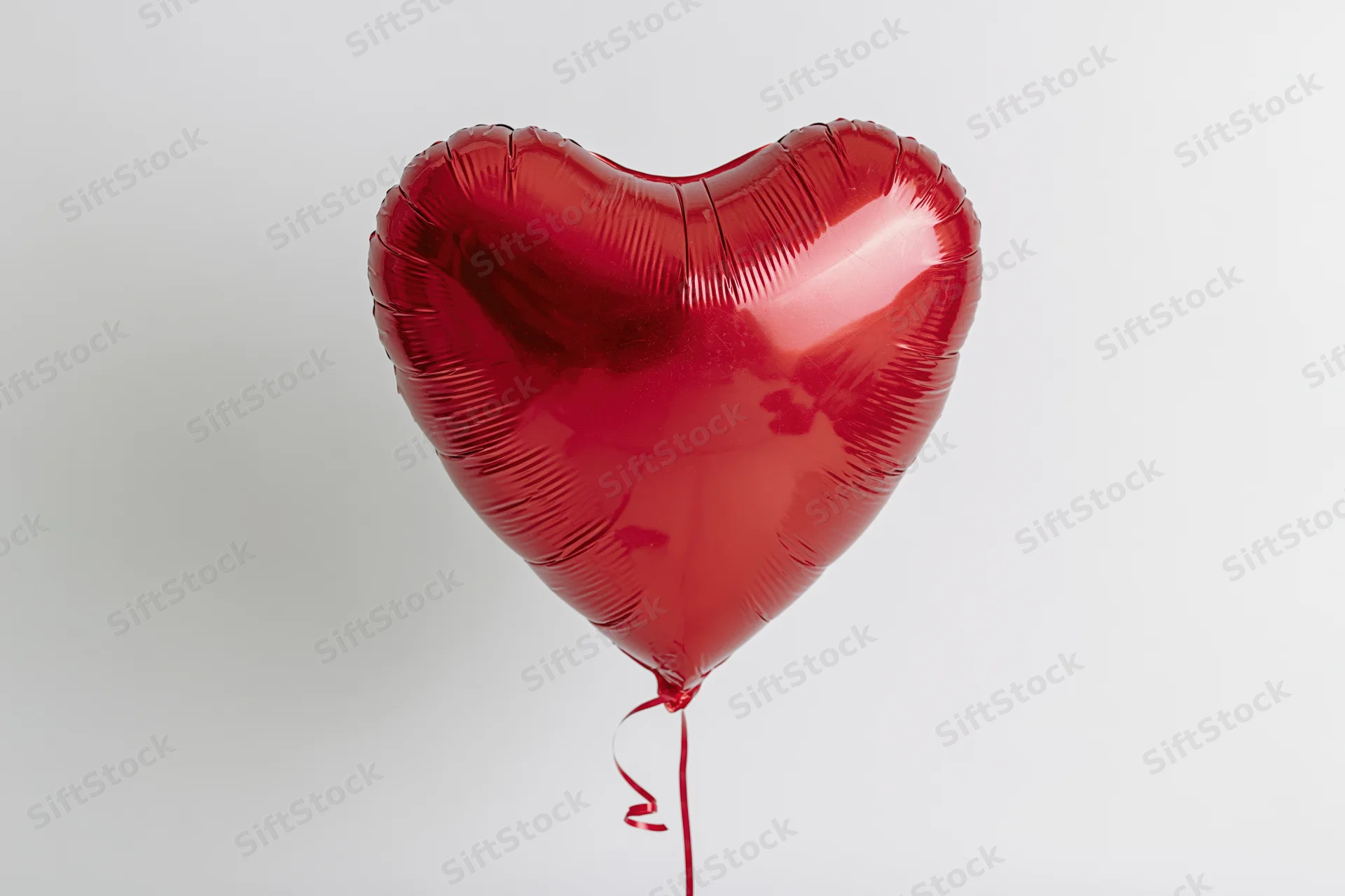 Red metallic heart-shaped foil balloon floating against a plain white background