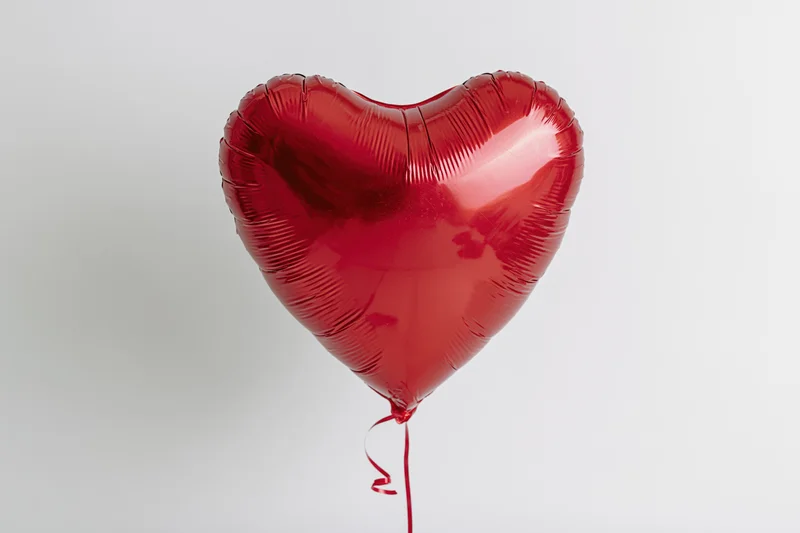 Red metallic heart-shaped foil balloon floating against a plain white background