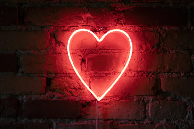 Red neon heart sign glowing on dark brick wall
