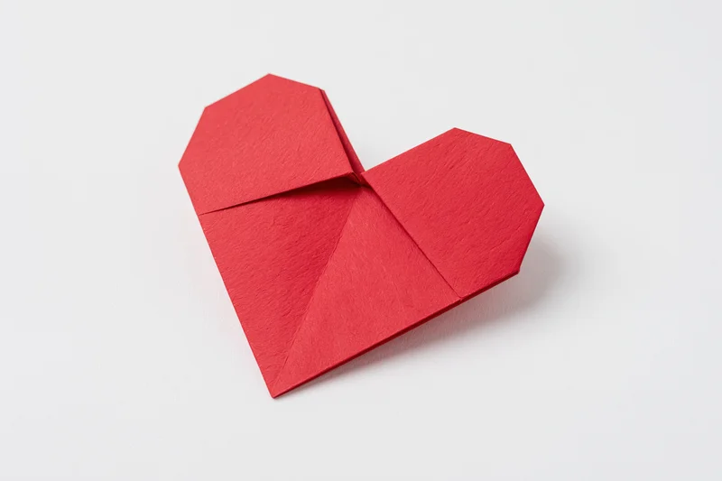 Red origami heart made from folded paper centered on white background