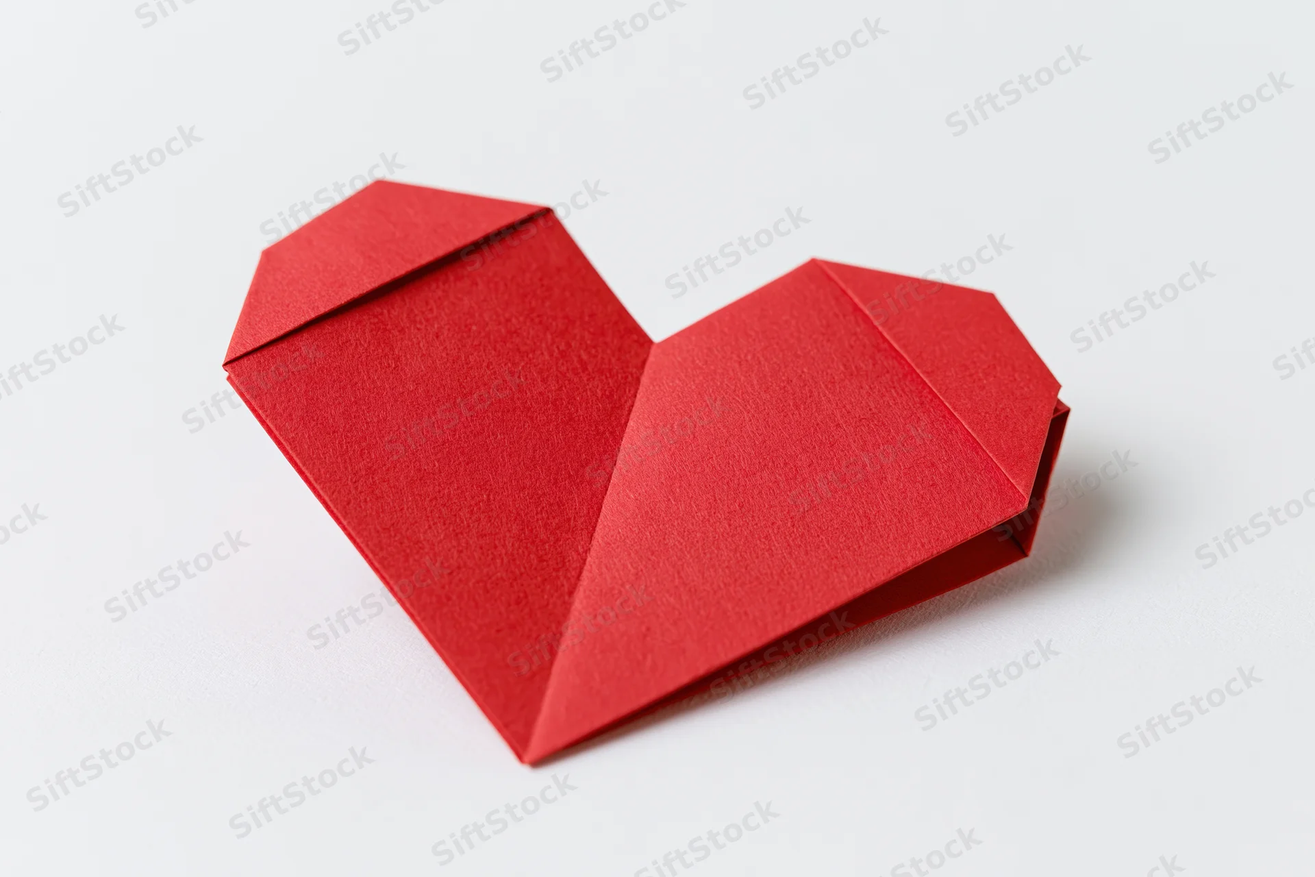 Red origami heart made from folded paper on a white background