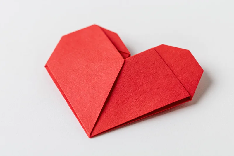 Red origami heart made from folded paper on white background