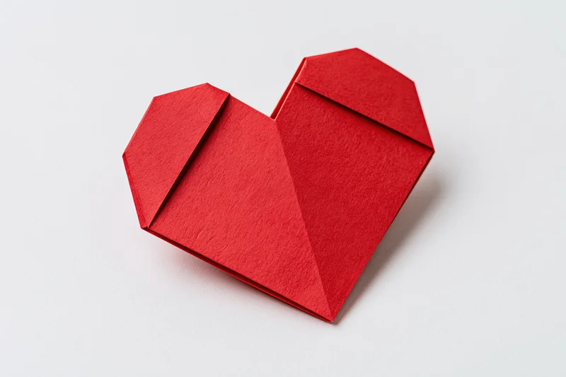 Red origami heart made from folded paper centered on a white background