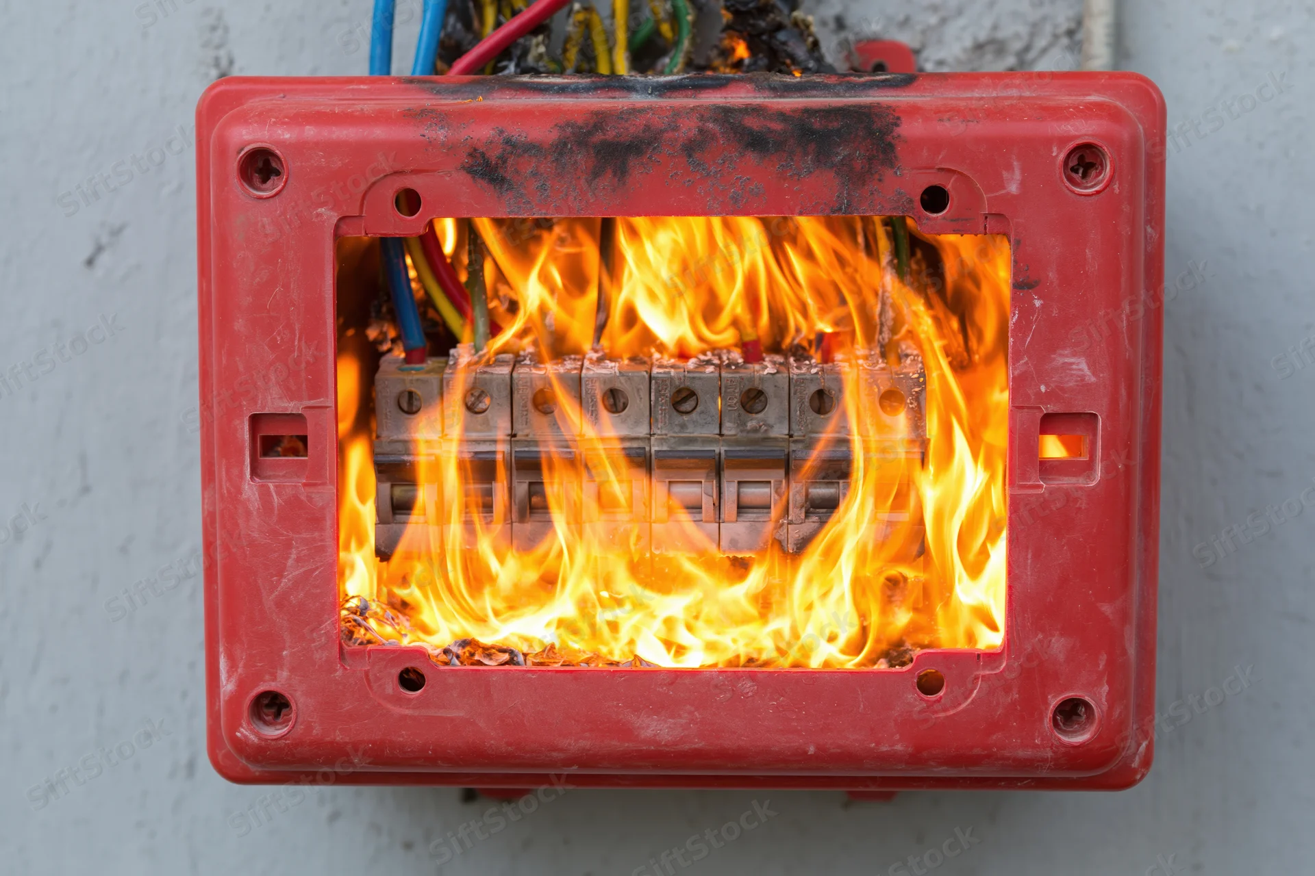 Burning electrical fuse box with flames and melted plastic on concrete wall