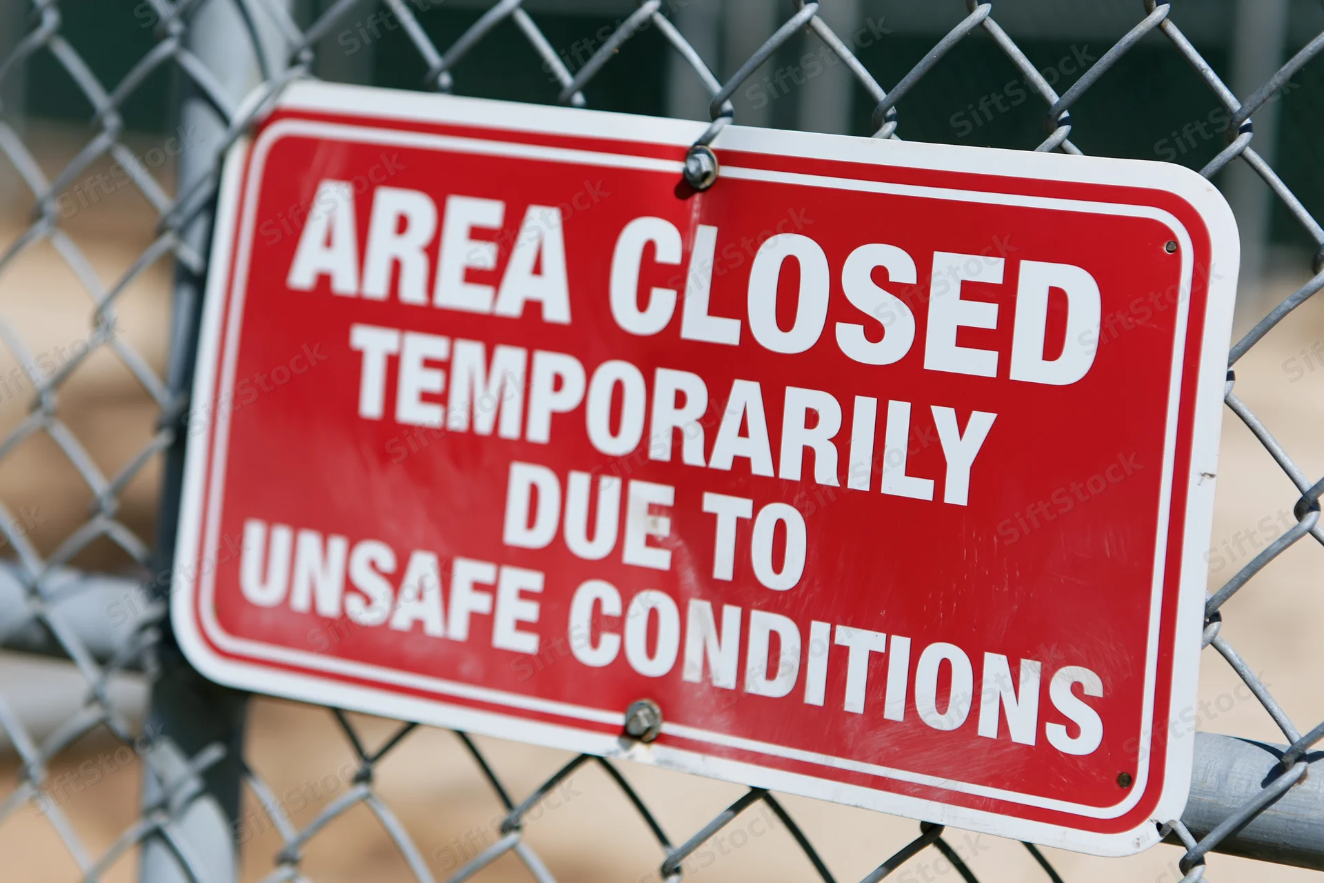 Red warning sign reading area closed temporarily due to unsafe conditions attached to chainlink fence