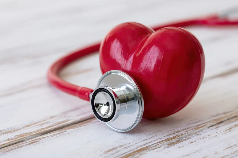 Red heart model with stethoscope chest piece resting on white wooden surface