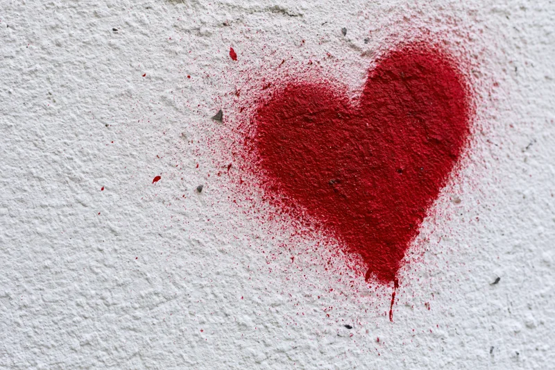 Red spray-painted heart graffiti on a rough white concrete wall