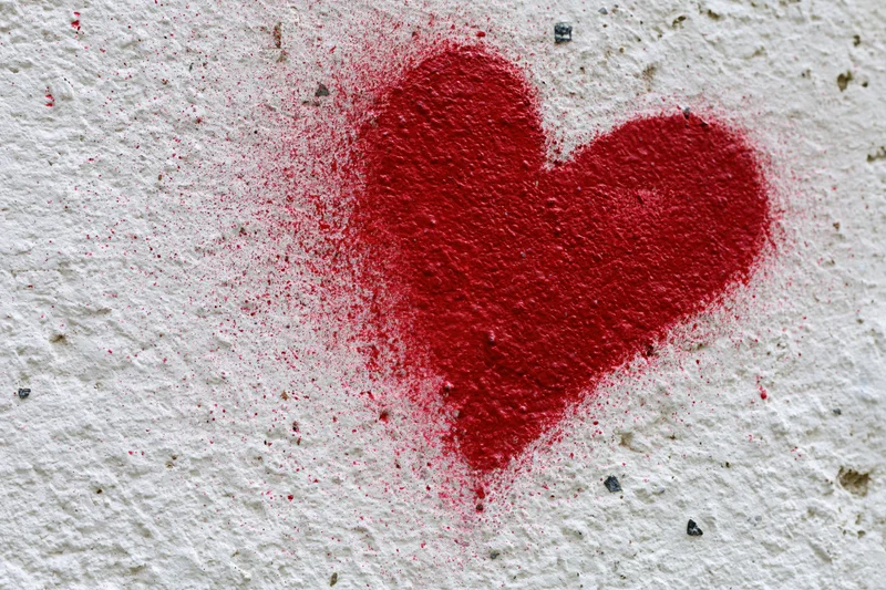 Red spray-painted heart graffiti on a rough white concrete wall