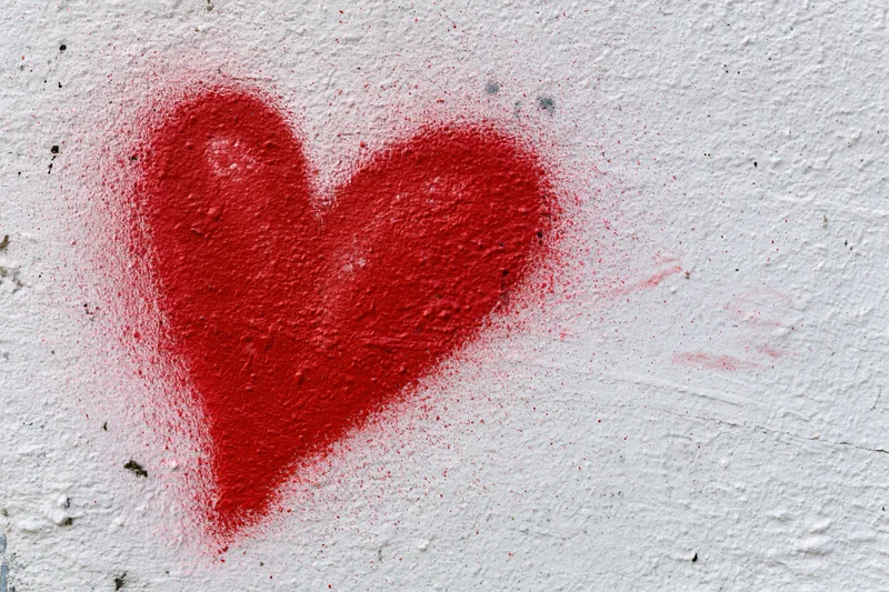 Red spray-painted heart graffiti on a rough white concrete wall