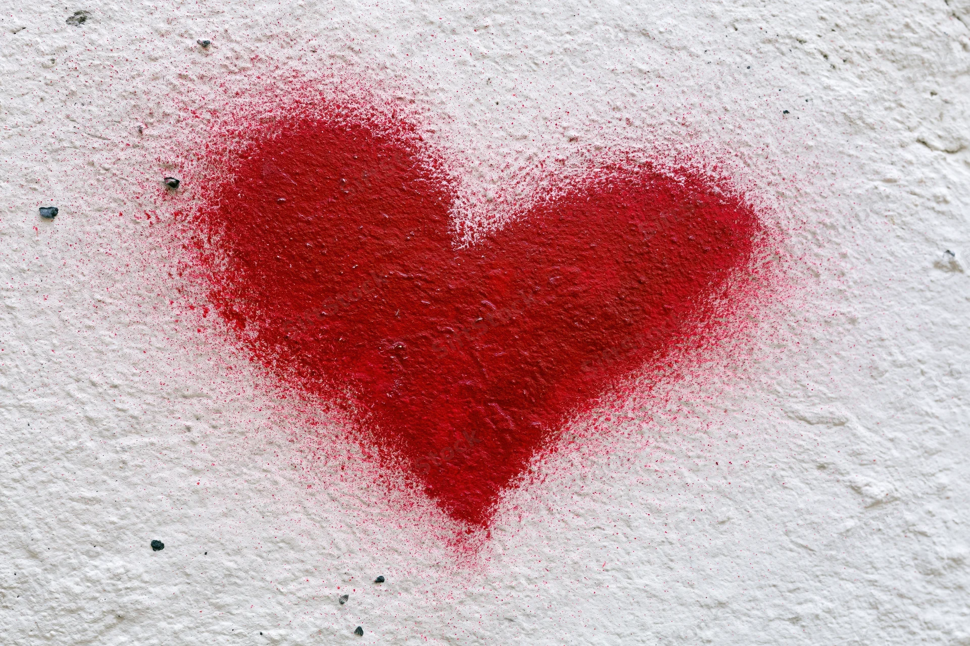 Red spray-painted heart graffiti on a rough white concrete wall