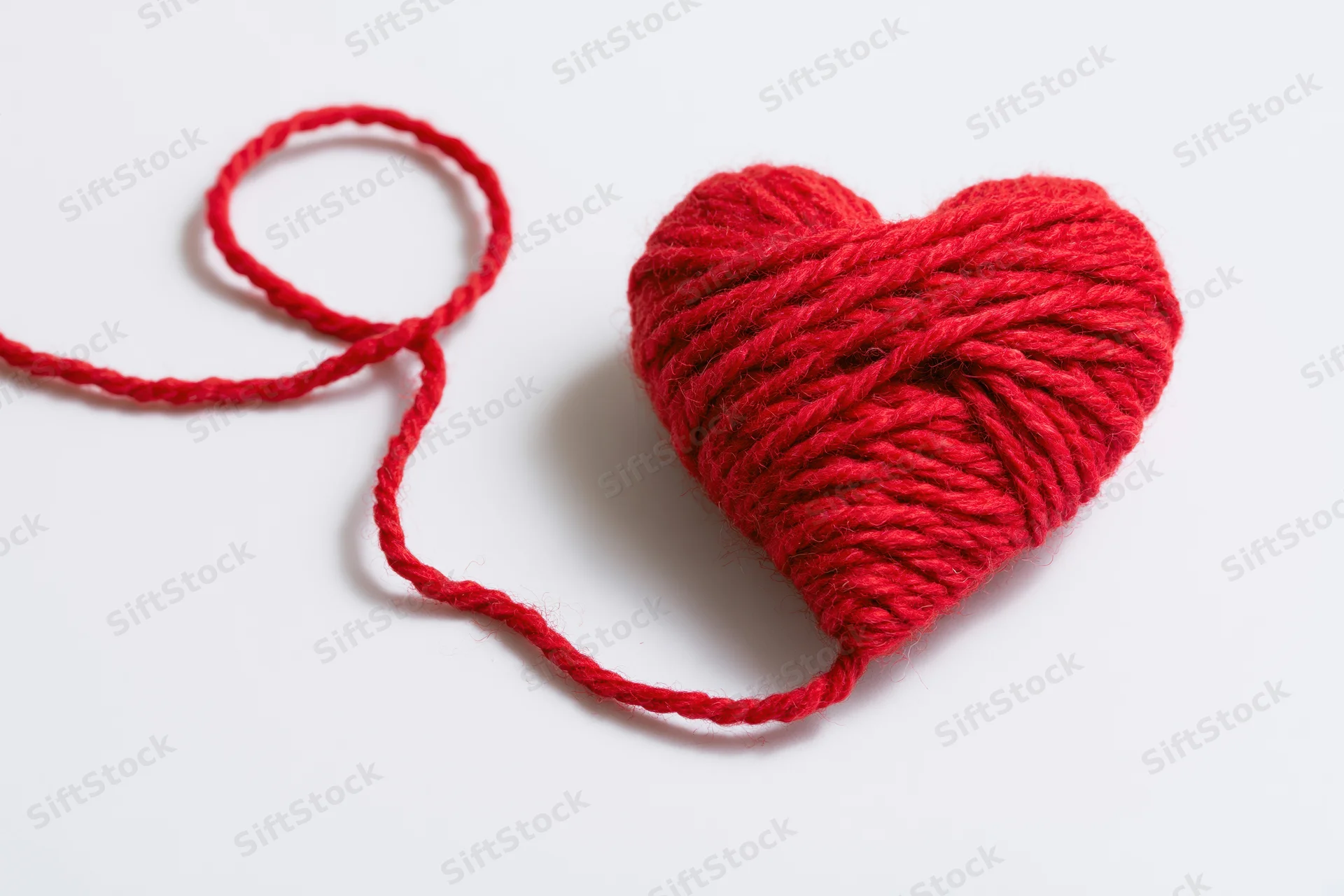 Red wool yarn wound into a heart shape resting on a white surface