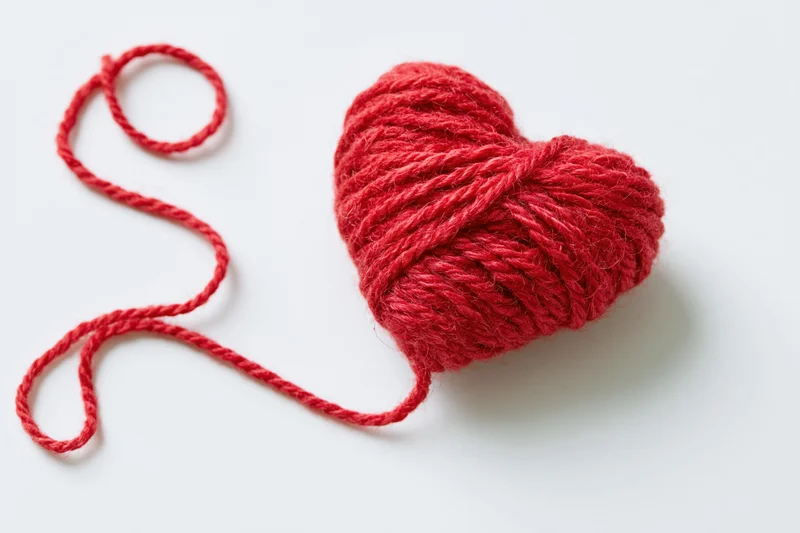 Red wool yarn wound into a heart shape on white background
