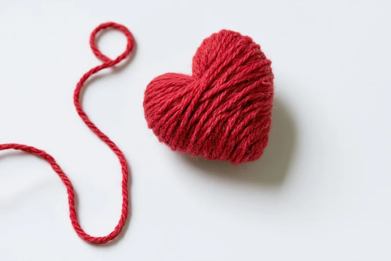 Red wool yarn wound into a heart shape resting on a white surface