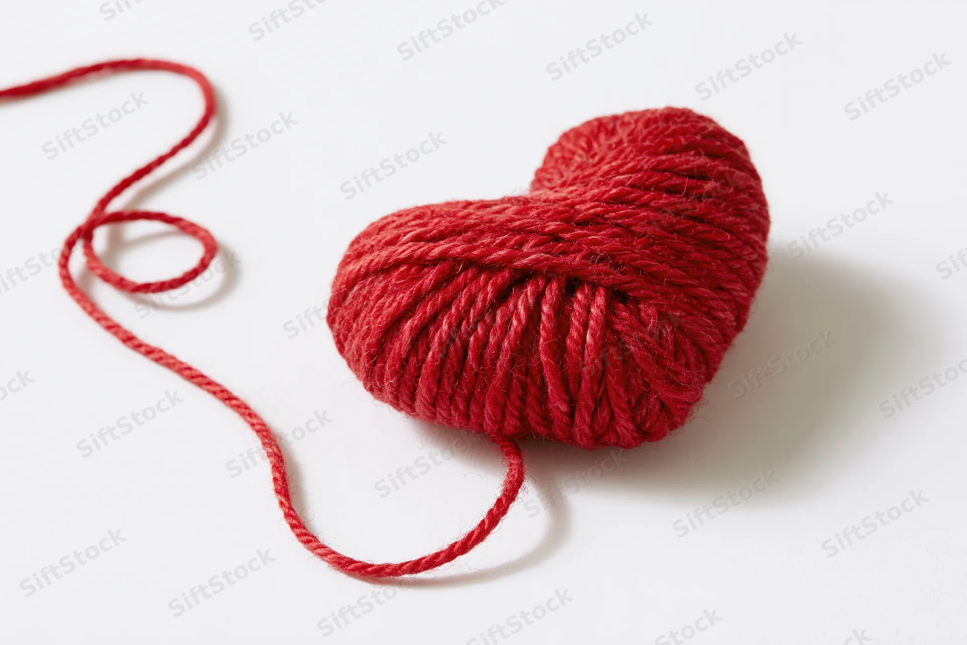 Red wool yarn wound into a heart shape on white background