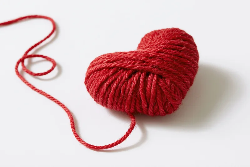 Red wool yarn wound into a heart shape on white background