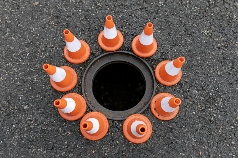 Small orange and white traffic cones arranged in a circle around a manhole on asphalt pavement