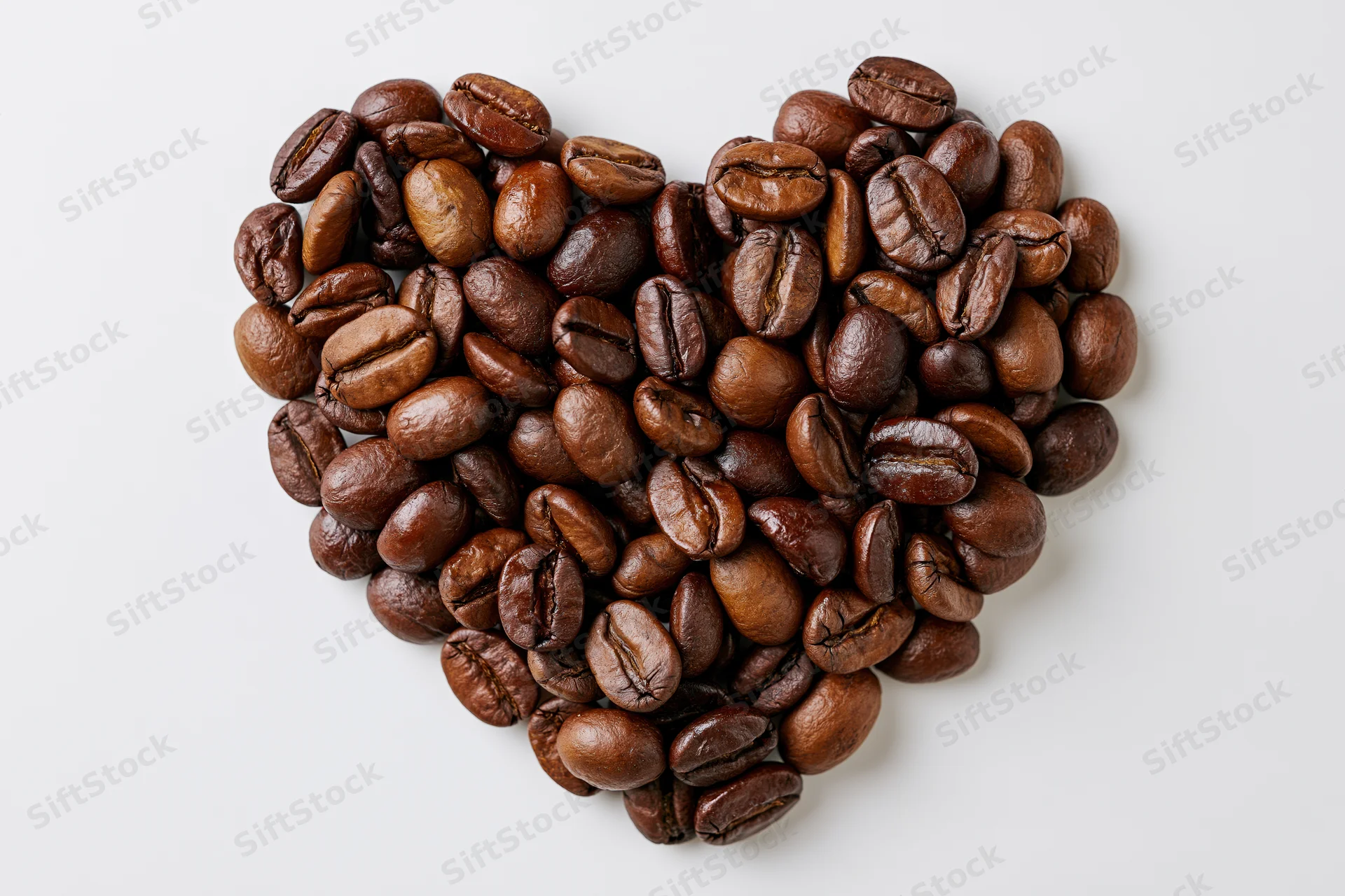 Roasted coffee beans arranged in heart shape on white background
