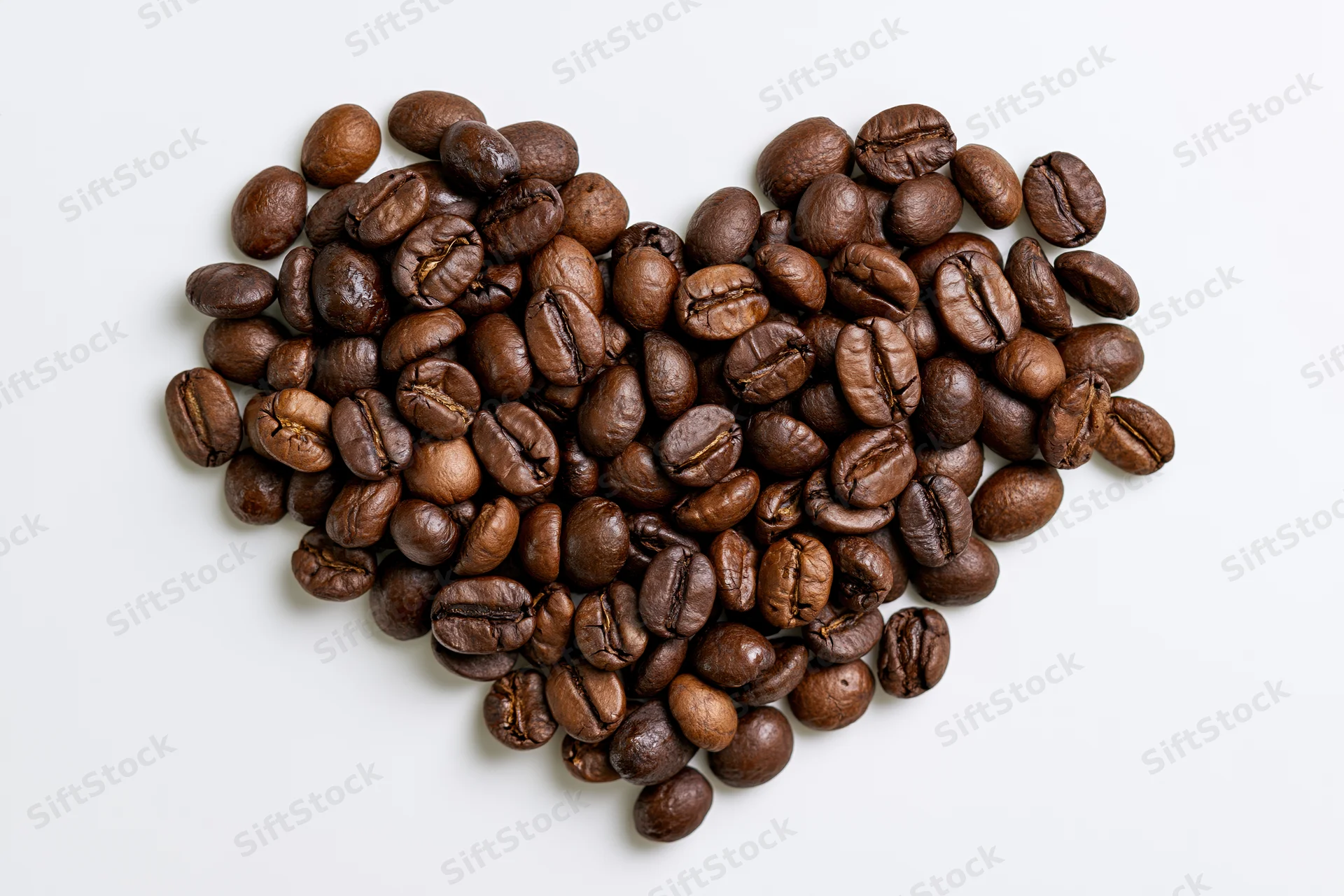 Roasted coffee beans arranged in heart shape on white background