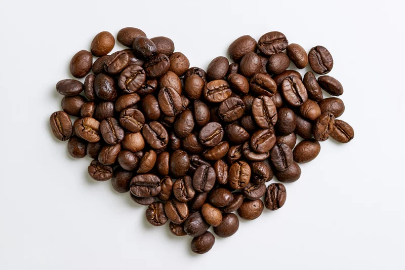 Roasted coffee beans arranged in heart shape on white background