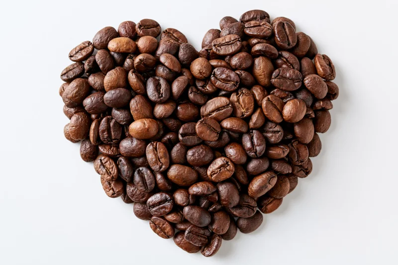Roasted coffee beans arranged in heart shape on white background