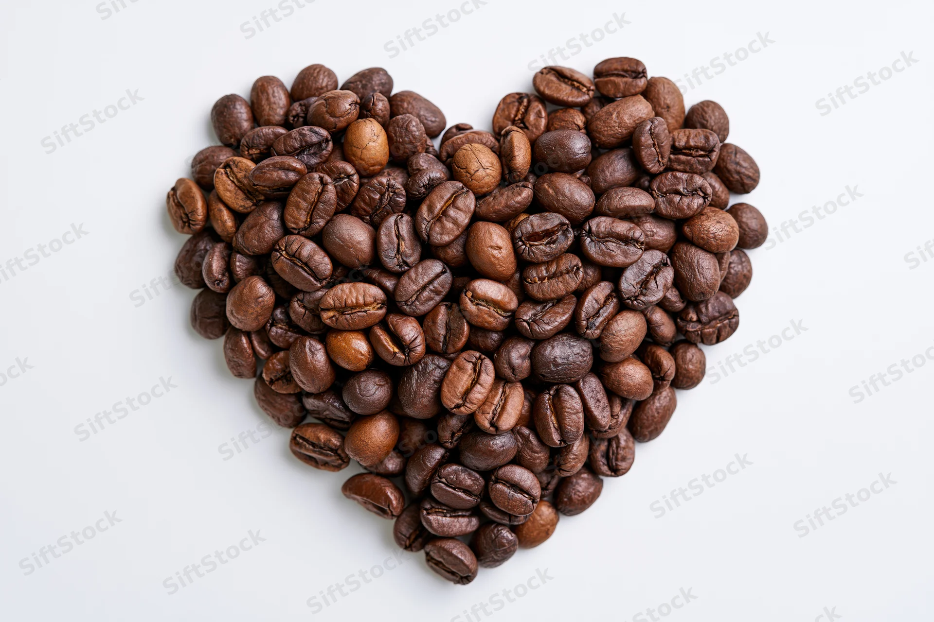 Roasted coffee beans arranged in heart shape on white background