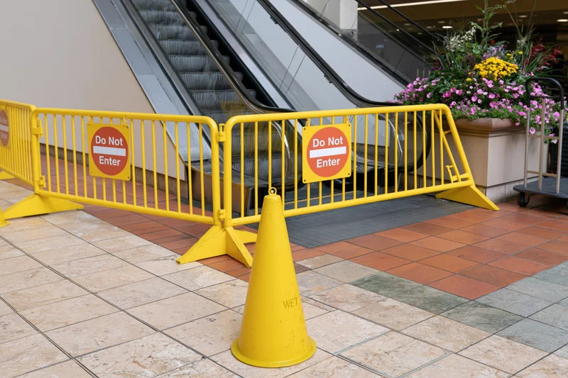 Yellow safety barriers with do not enter signs blocking escalator in shopping mall interior
