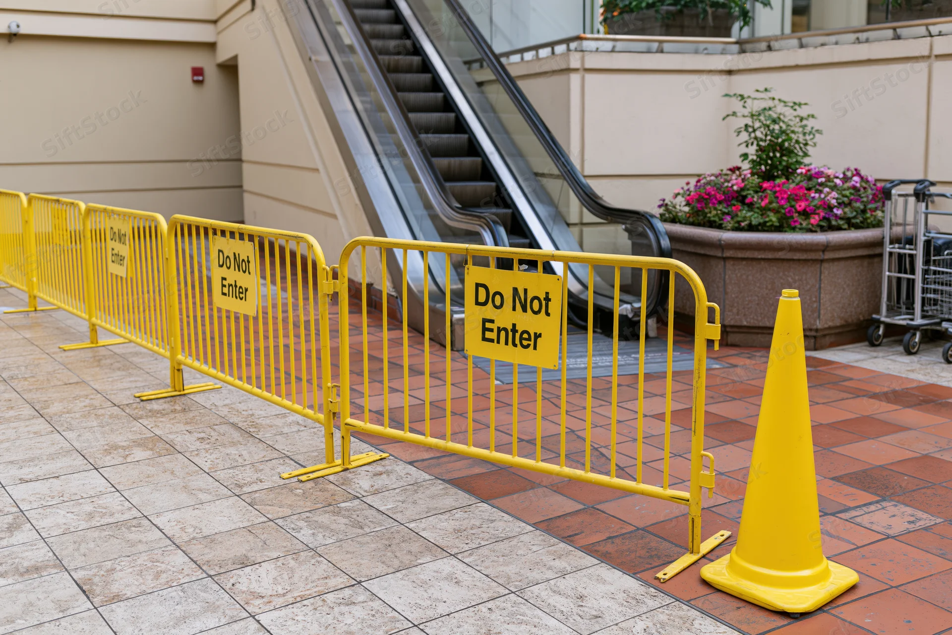 Row of yellow safety barriers with do not enter signs blocking escalator in indoor shopping area