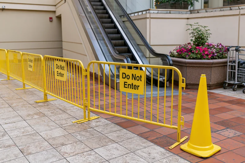 Row of yellow safety barriers with do not enter signs blocking escalator in indoor shopping area