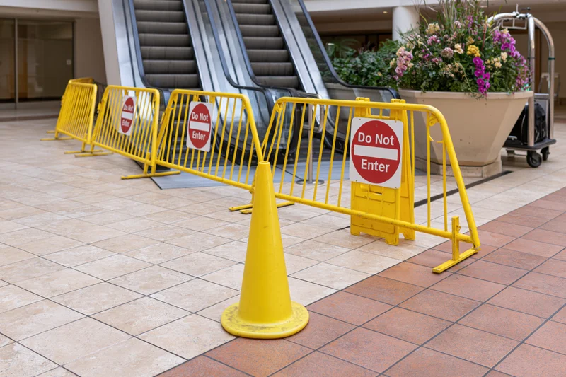 Row of yellow safety barriers with do not enter signs blocking escalator in shopping mall interior