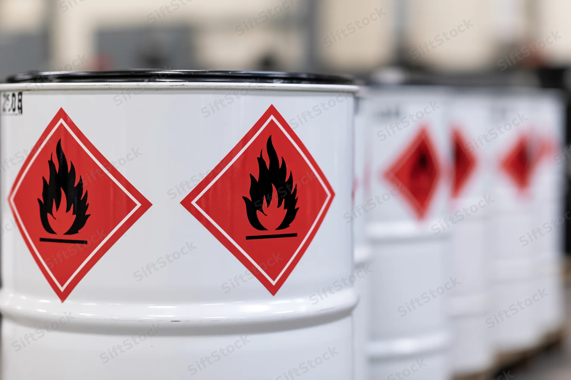 Row of white industrial drums with flammable hazard symbols in a warehouse